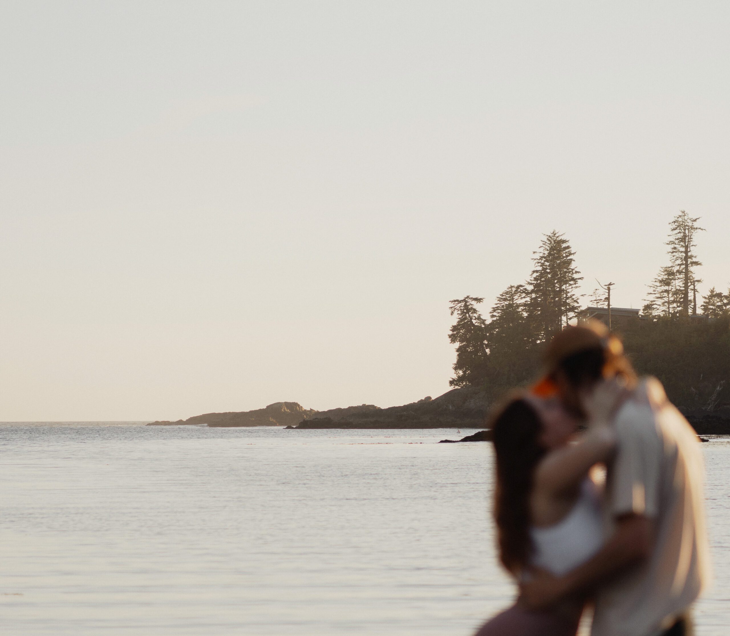 Couple kissing with the ocean and islands in focus behind them during a couples session at Little Beach in Ucluelet by Latitude 49 photography