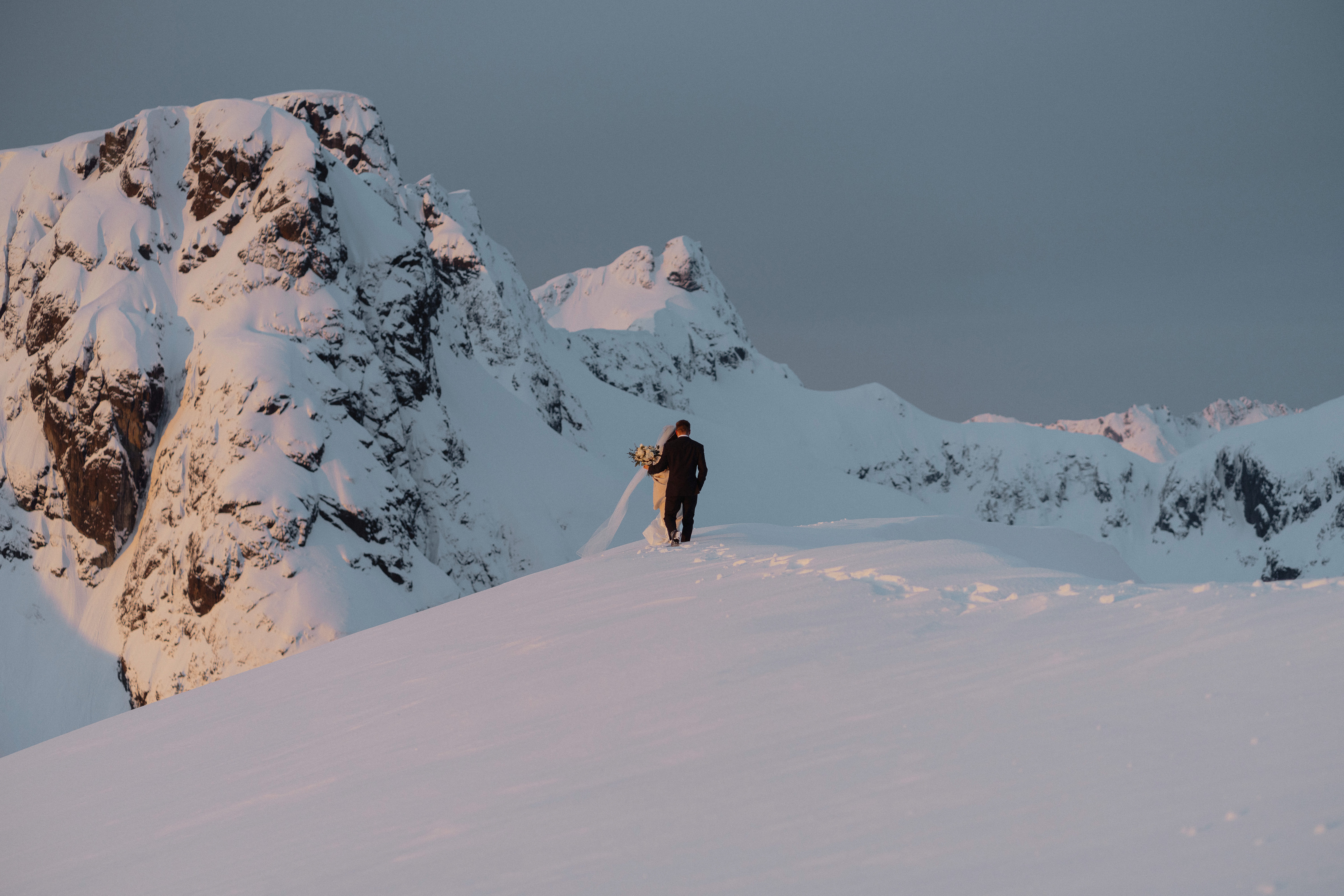 Bride and groom walking in the snow during their helicopter elopement at sunrise near the Comox Glacier by latitude 49 photography