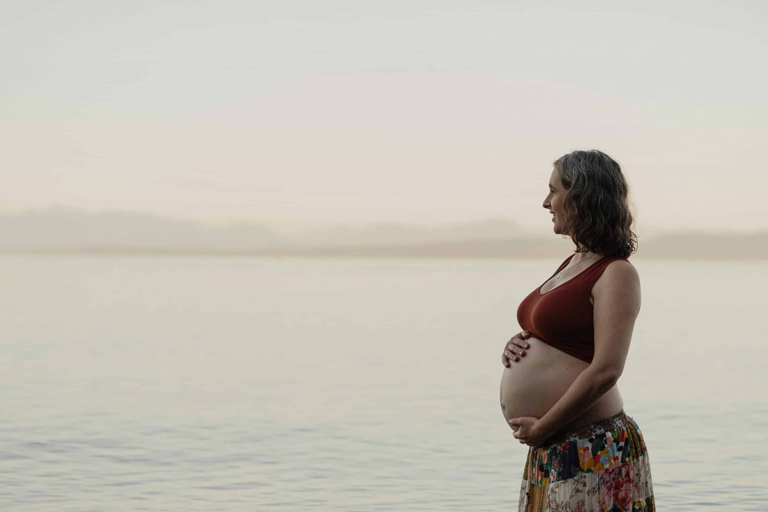 New expecting mom standing in the ocean during golden hour maternity portraits