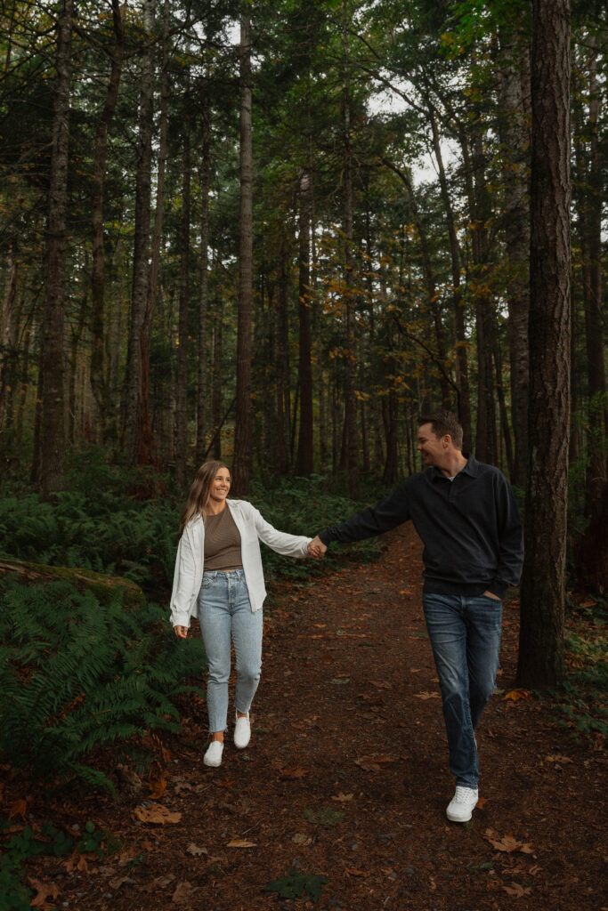 Couple during their engagement session in  the tall trees and ferns of Seal Bay Park in Courtenay by Latitude 49 Photography