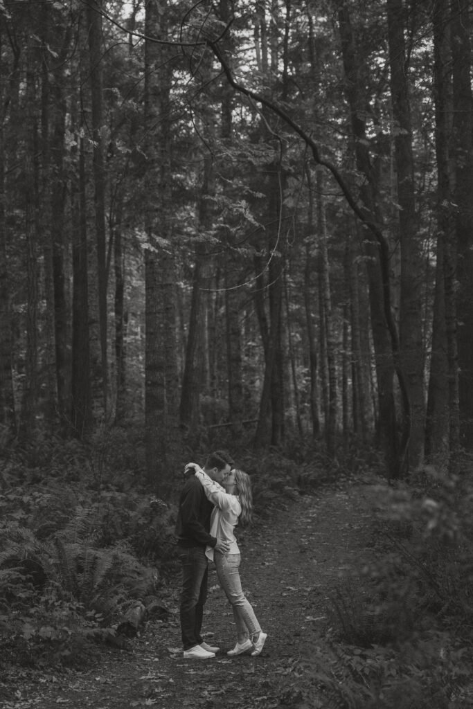 Couple during their engagement session in  the tall trees and ferns of Seal Bay Park in Courtenay by Latitude 49 Photography