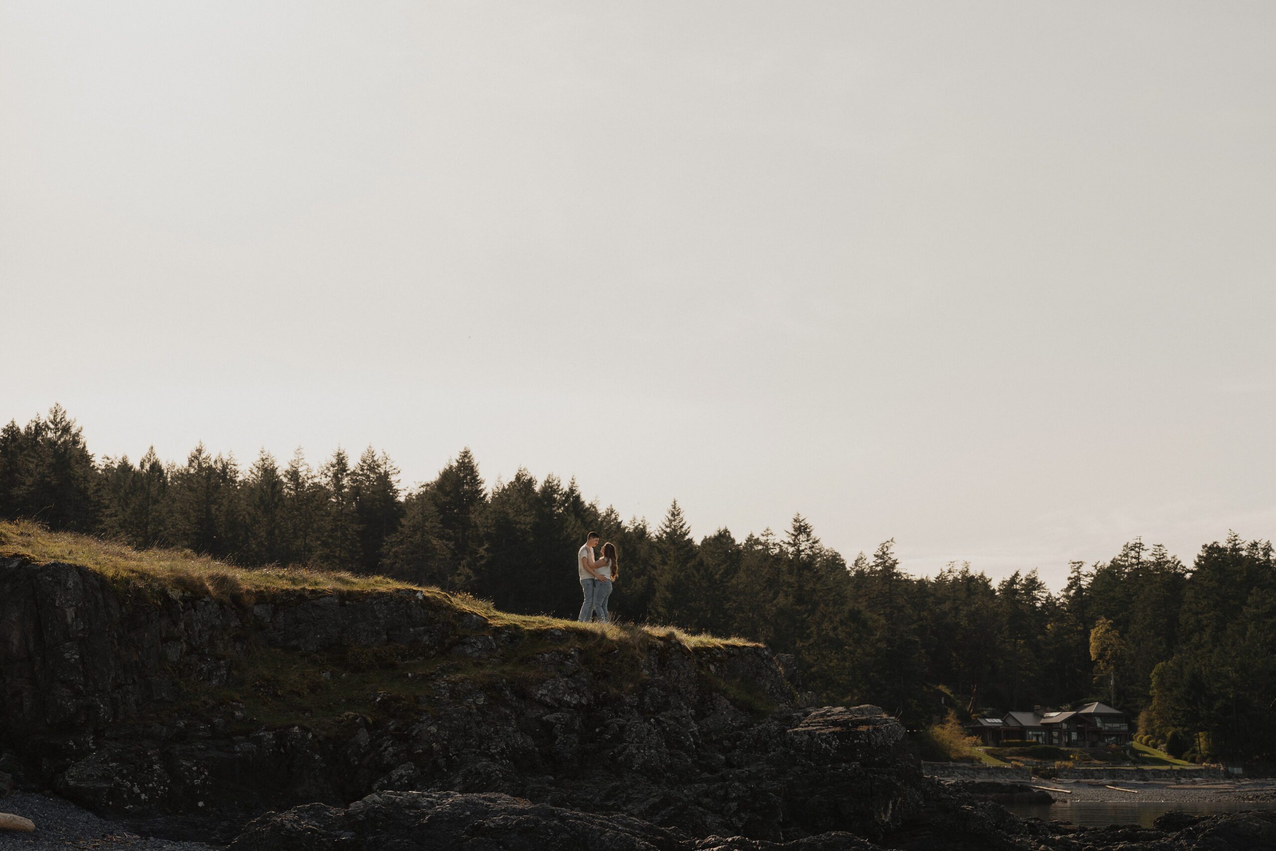 Dakota and James holding each other at Es-hw Sme~nts Community park during their engagement session at golden hour