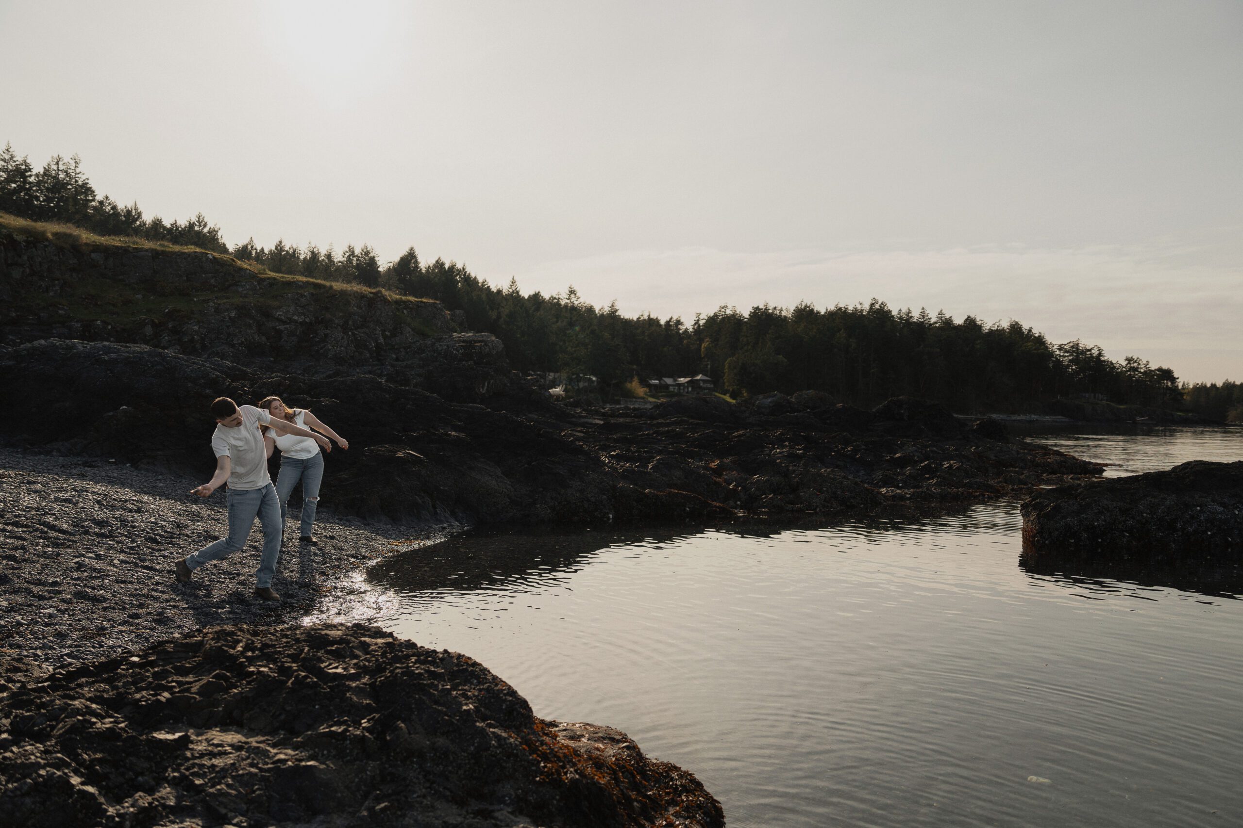 Engaged couple skipping rocks during their engagement session at Es-hw Sme~nts Community Park in Nanoose