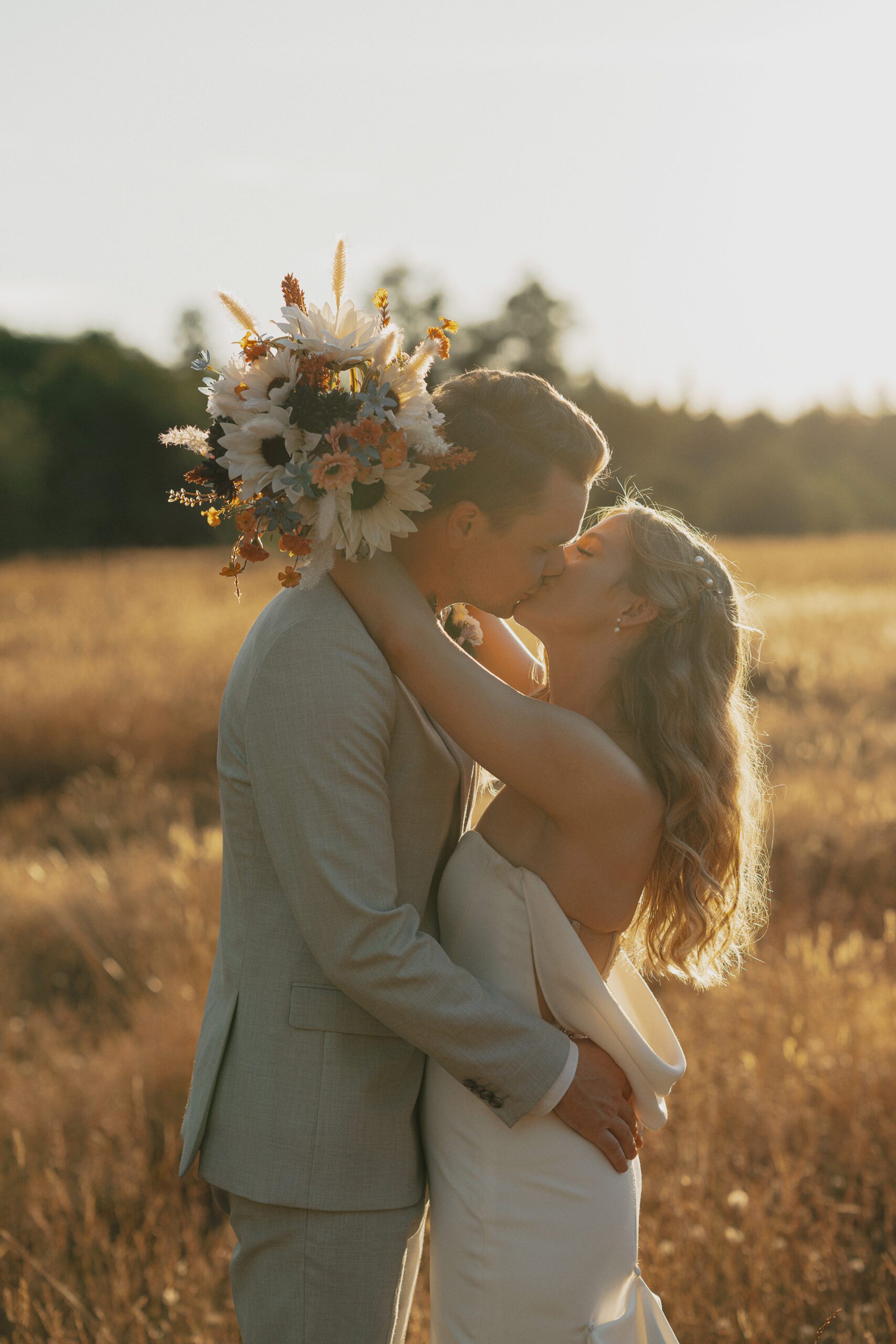 bride and groom kissing in a field at golden hour during wedding portraits in Comox by latitude 49 Photography