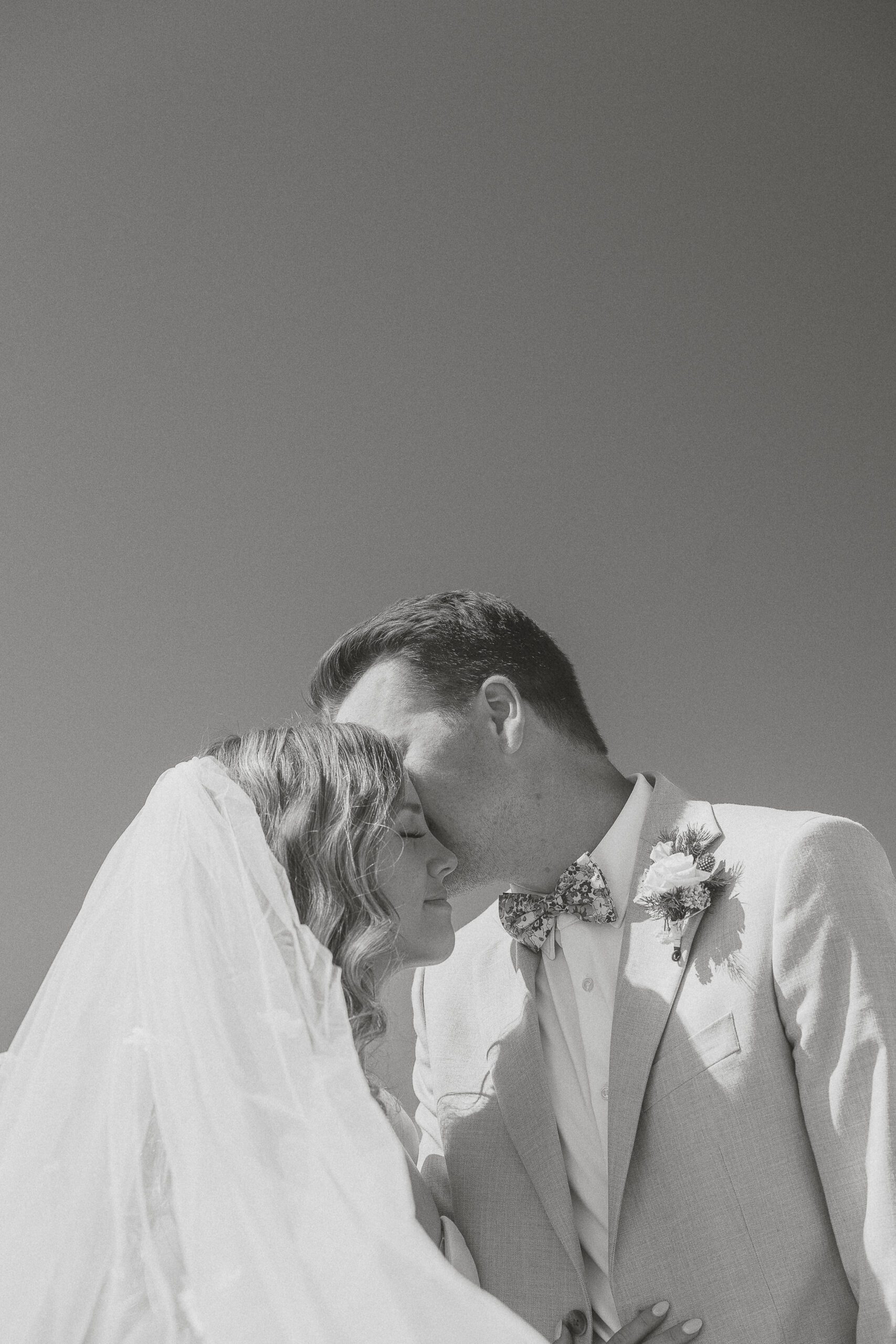 bride and groom kissing with a windswept veil during their wedding portraits at Airforce Beach in Comox by Latitude 49 Photography