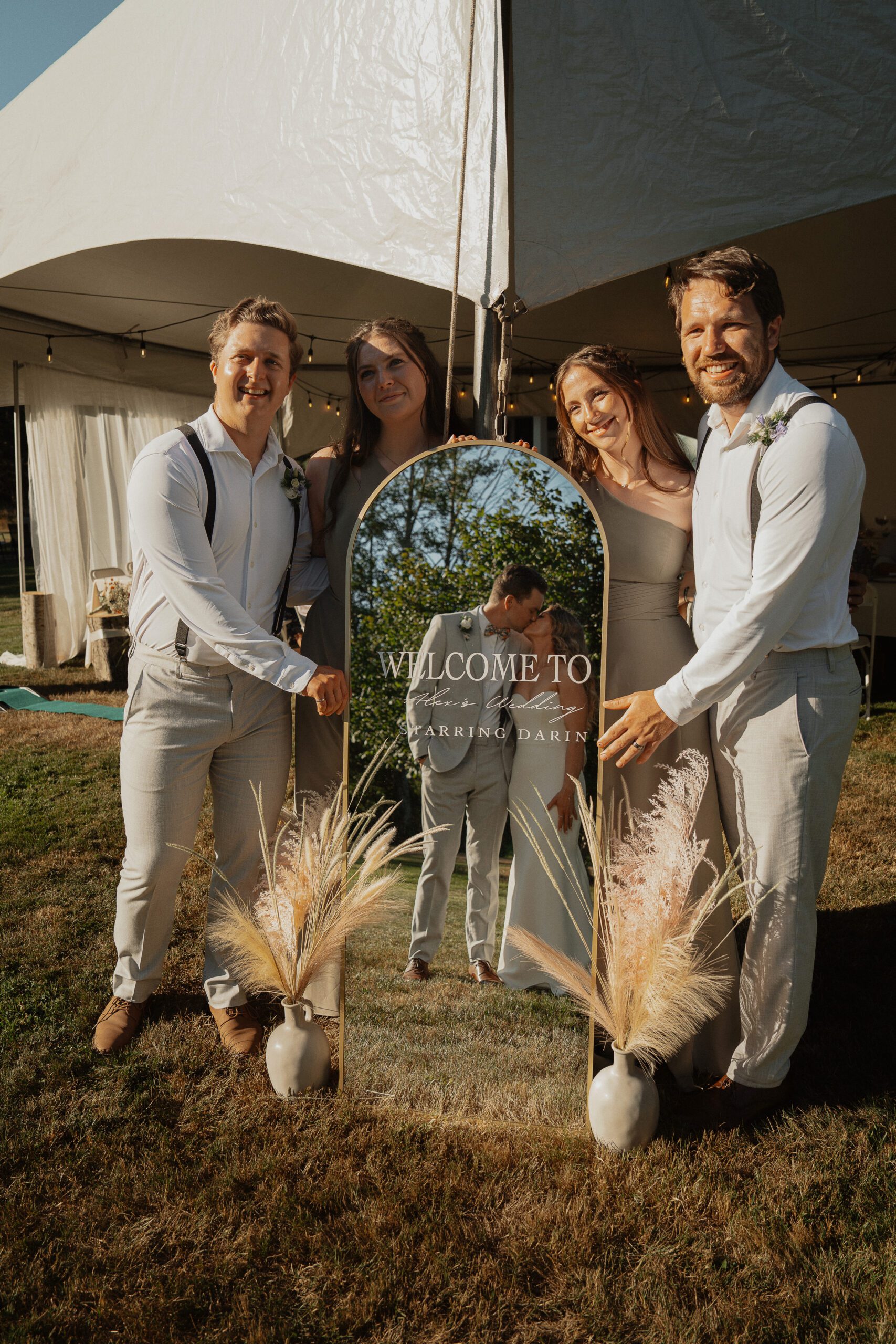 Bride and groom kissing in their wedding mirror with their wedding party behind it in comox during their wedding portraits by Latitude 49 photography