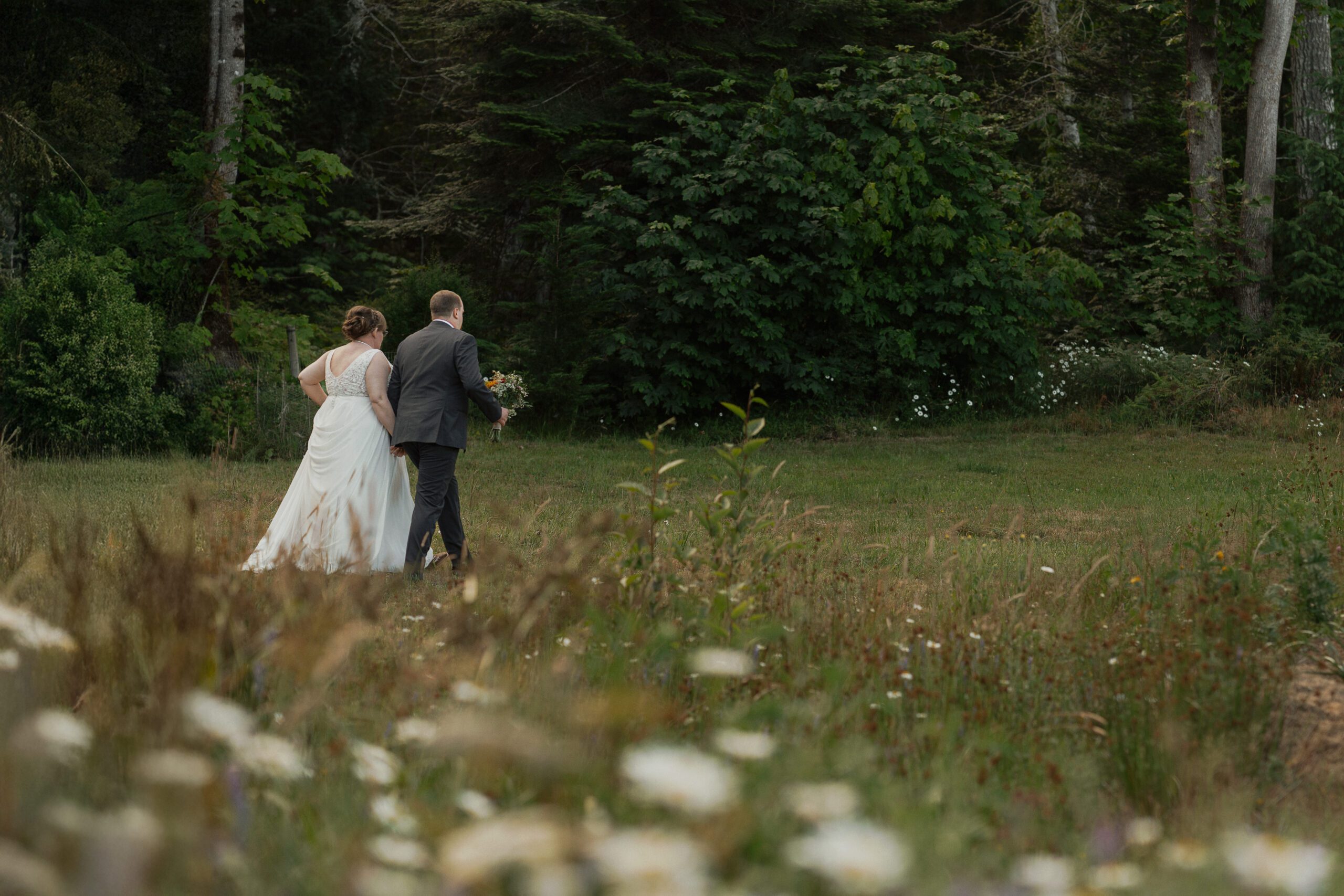 Cassie and Jon walking in a field of wildflowers during their wedding portraits in Union Bay by Latitude 49 photography