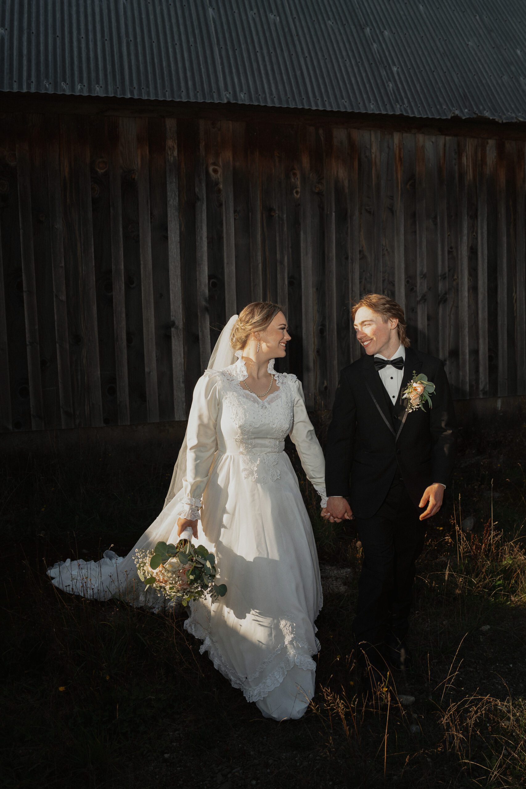 Bride and groom walking in front of an old barn during their wedding portraits in the Comox Valley by Latitude 49 Photography