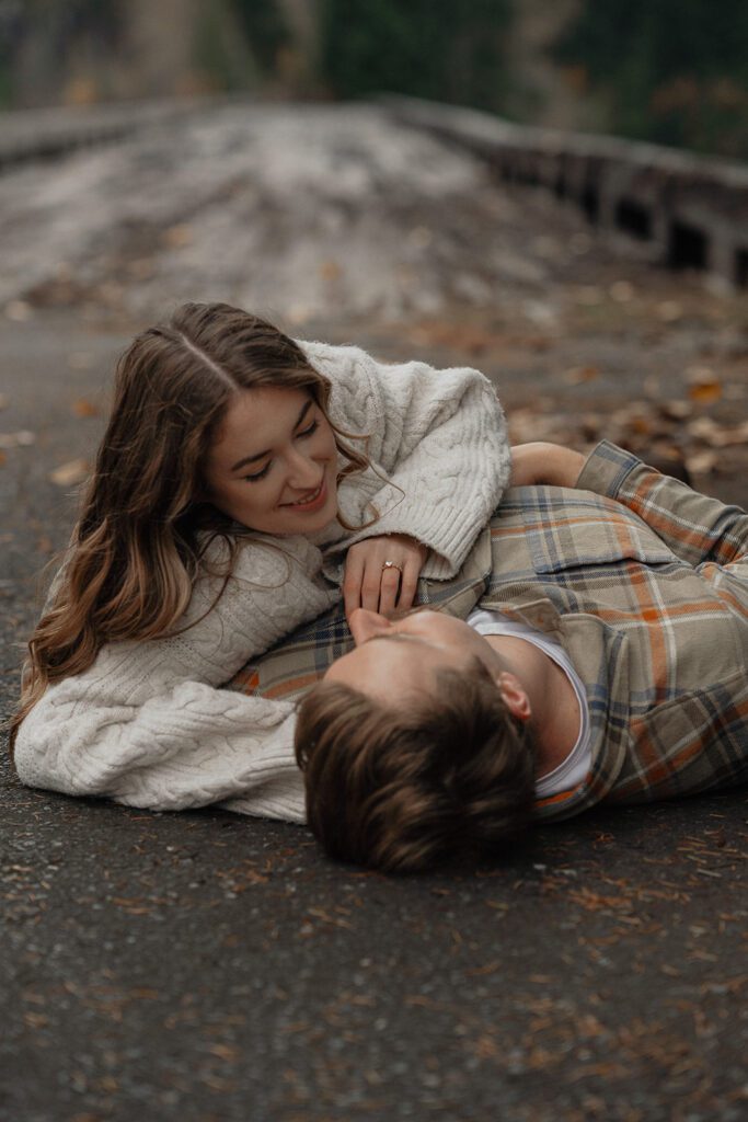 Liz looking longingly into connors eyes while laying on the ground during their fall engagement session at the Trestle Bridge in Campbell River.