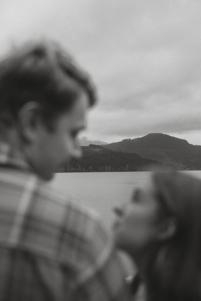 Liz and connor looking at each other with the mountainscape in focus in front of them during their fall engagement session at the Trestle Bridge in Campbell River.