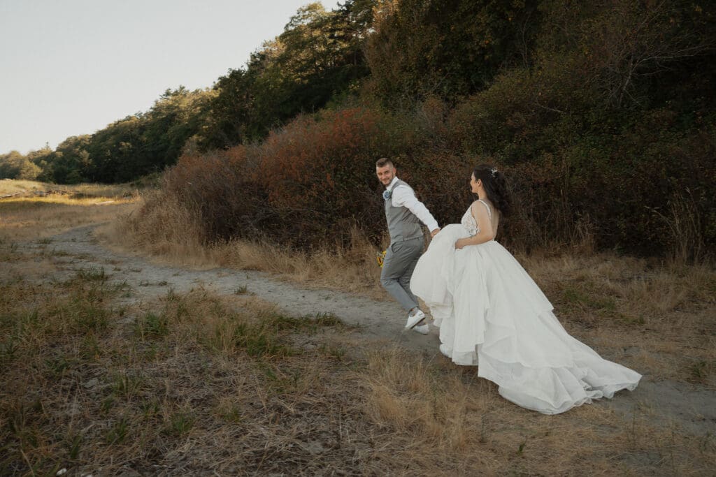 Bride and groom running in a field at Airforce Beach