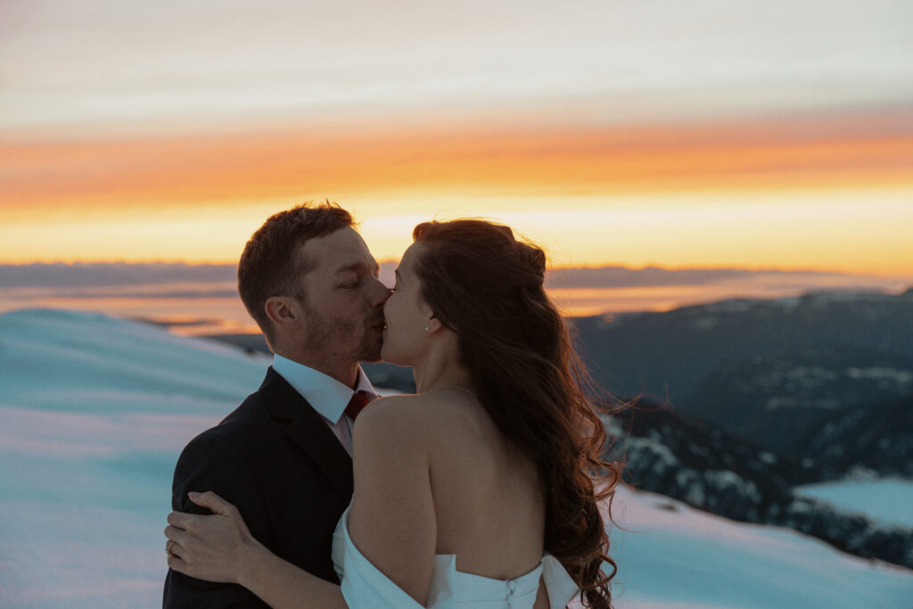 bride and groom share their first kiss on a mountain top